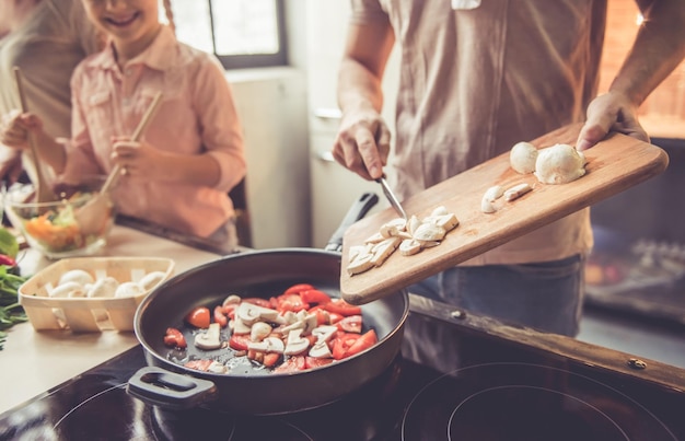 Abgeschnittenes Bild eines süßen kleinen Mädchens und ihrer schönen Eltern, die zu Hause zusammen in der Küche kochen