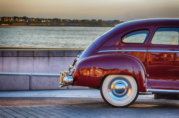 Abgeschnittenes Bild eines Vintage-Autos auf der Straße am Fluss gegen den Himmel bei Sonnenuntergang