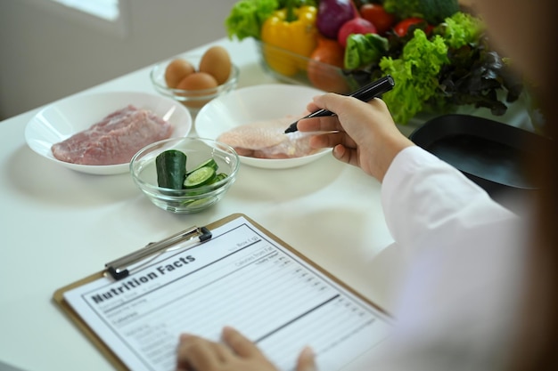 Abgeschnittenes Bild von einem Ernährungsberater in Laborkleidung, der eine gesunde Ernährung verschreibt oder einen Mahlzeitplan für einen Patienten in der Klinik erstellt