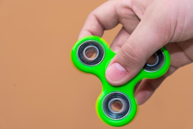 Abgeschnittenes Bild von einer Hand, die einen Fidget-Spinner vor braunem Hintergrund hält