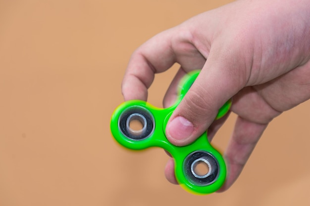 Foto abgeschnittenes bild von einer hand, die einen fidget-spinner vor braunem hintergrund hält