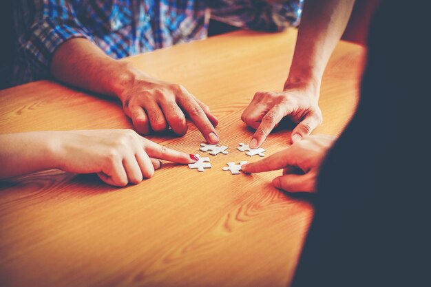 Foto abgeschnittenes bild von freunden, die an einem tisch puzzle spielen