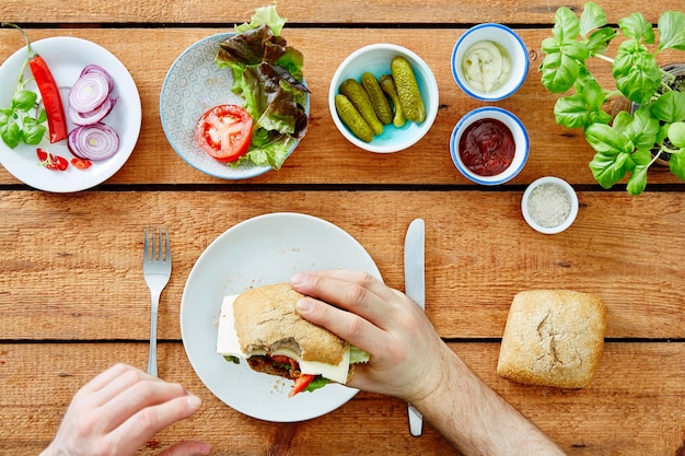 Abgeschnittenes Bild von Händen, die ein Sandwich am Tisch halten