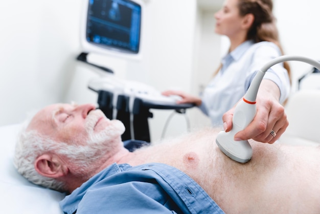 Abgeschnittenes Foto einer älteren männlichen Patienten bei einer Herzuntersuchung mit Ultraschall durch eine Arztin