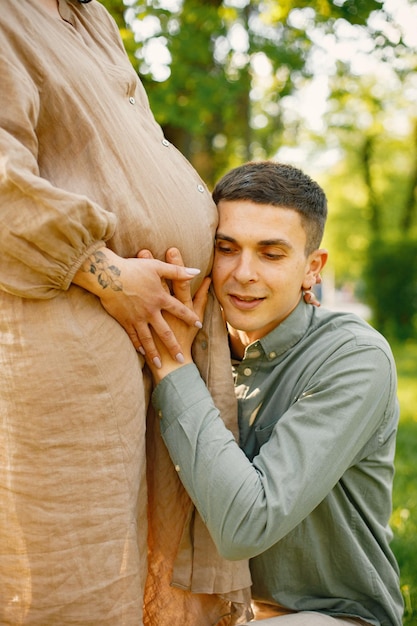 Abgeschnittenes Foto eines Mannes, der den schwangeren Bauch seiner Frau im Park umarmt