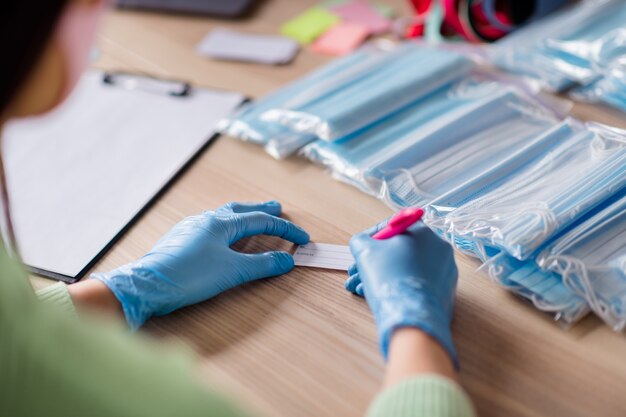 Abgeschnittenes Foto von Damenhänden Latexhandschuhe Trendgeschäft Organisation der Verpackung medizinischer Gesichtsmasken für die Grippe Eigenes Produkt Bestellung schreiben Adresse prüfen Sets Lieferung Homeoffice drinnen vorbereiten