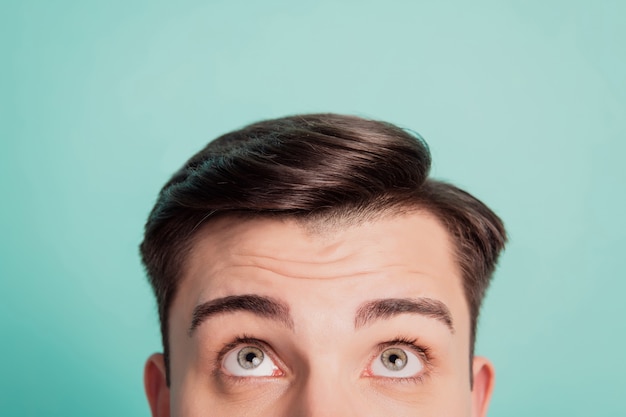 Abgeschnittenes Nahaufnahmeporträt eines neugierigen Kerls, der leere Leerstellen auf blaugrünem Hintergrund nachschlägt