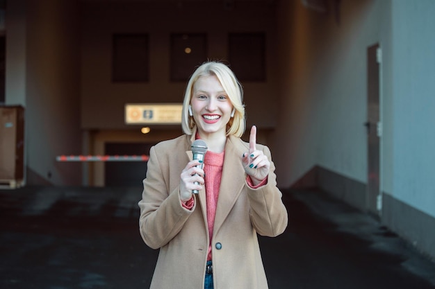 Abgeschnittenes Porträt einer professionellen Reporterin bei der Arbeit Junge Frau, die mit einem Mikrofon in der Hand auf der Straße steht und in die Kamera lächelt Horizontaler Schuss Selektiver Fokus auf Frau