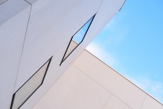 Abgewinkelter Blick auf das Äußere des hohen Gebäudes an einem sonnigen Tag Konzept des modernen weißen Gehäuses mit reflektierenden Fenstern vor blauem Himmel Abstrakter Hintergrund der Architektur für Kopienraum außerhalb