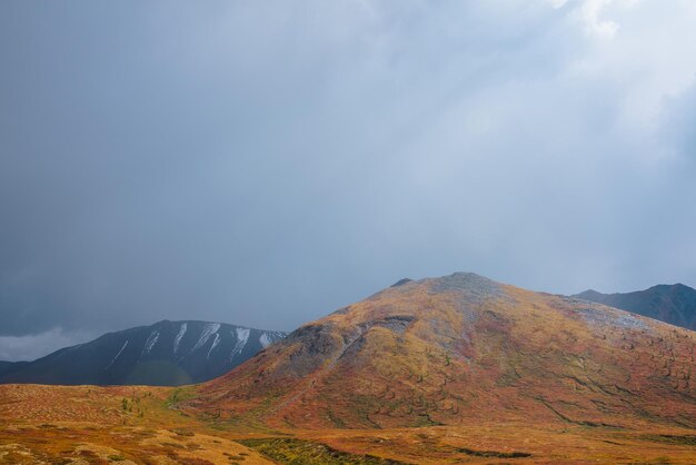 Foto abigarrado paisaje otoñal con colina iluminada por el sol y silueta de cordillera durante la lluvia colores otoñales vivos en las montañas rayos de sol en un cielo espectacular sobre una colina multicolor bajo la luz del sol rayos de sol en el cielo gris