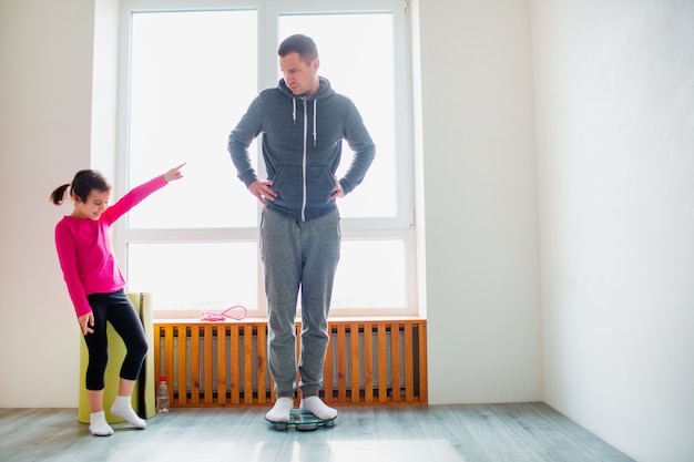 Abnehmen. Vater und Tochter werden auf Haushaltswaagen gewogen. Lustige und freudige Momente, die Spaß in der Familie haben. Diät, richtige Ernährung und gesundes Lebensstilkonzept.