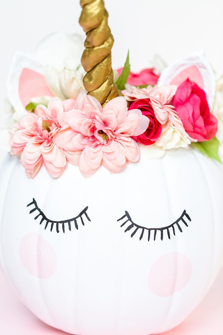 Foto abóbora artesanal pintada de branco e decorada com flores cor de rosa como unicórnio em fundo branco.