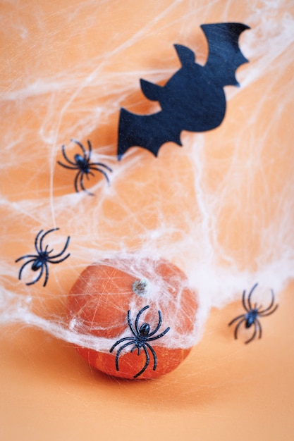 Abóbora de Halloween com morcego teia de aranha e aranhas pretas em fundo laranja