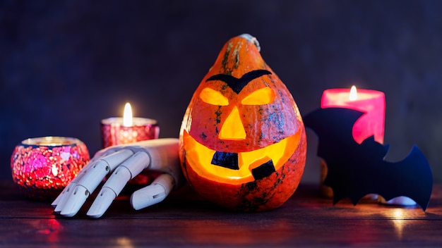 Abóbora de Halloween com velas acesas em um fundo escuro. Sorriso de abóbora de Halloween e olhos assustadores com uma mão de madeira. Conceito de halloween