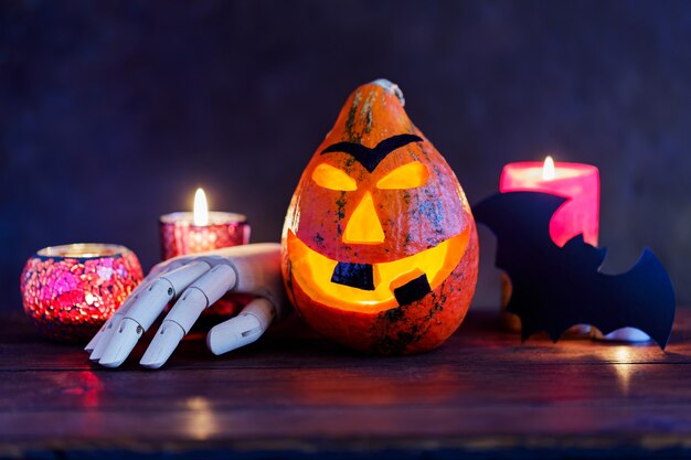 Abóbora de Halloween com velas acesas em um fundo escuro. Sorriso de abóbora de Halloween e olhos assustadores com uma mão de madeira. Conceito de halloween