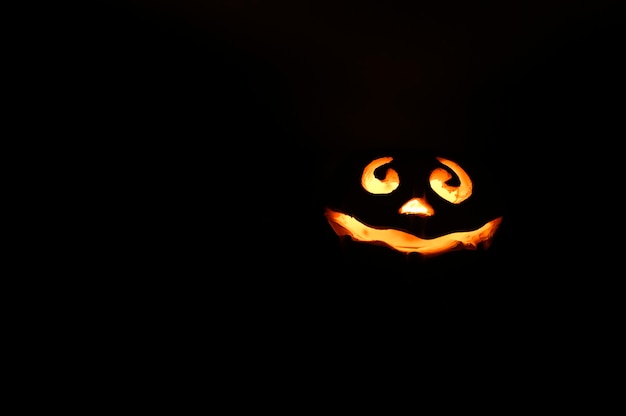 Abóbora de Halloween de rosto sorridente brilhante, suporte de vela, isolado em fundo preto escuro à noite. espaço para texto.