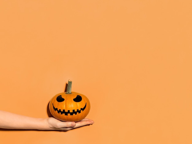 Abóbora de Halloween na mão em fundo laranja Conceito de Halloween com espaço de cópia para texto ou design Luz dura Jackolantern rosto rindo em abóbora laranja