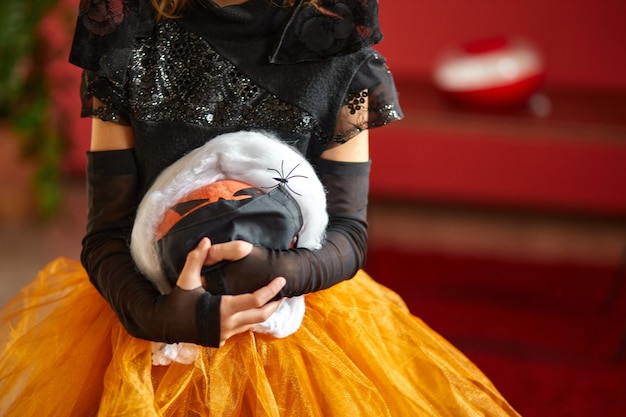 Foto abóbora de halloween na máscara de proteção médica preta nas mãos da menina.