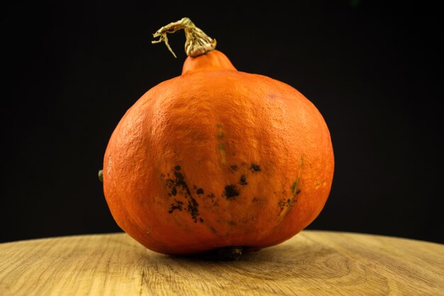 Foto abóbora de hokkaido laranja ou kuri vermelho em uma tábua de madeira em um fundo preto. foto de conceito de comida vegetal fresca de outono