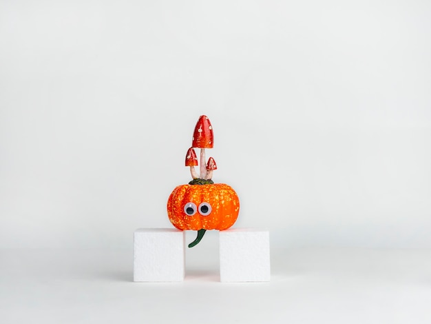 Abóbora engraçada com olhos e cogumelos em um cubo branco Conceito de Halloween Ideia criativa