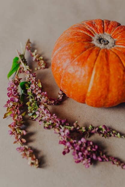 Abóbora laranja com fundo de papel kraft com flores de outono ao redor.