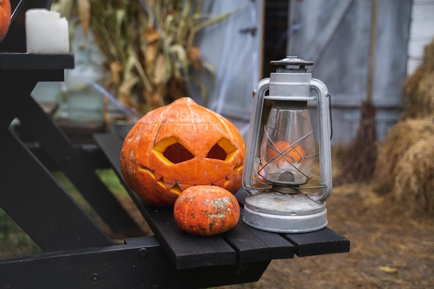 Abóbora laranja para o halloween no chapéu de bruxa preta jackolantern com boca de olhos esculpidos assustadoresVelas na mesa de madeira perto do celeiro DIY decoração de rua entretenimento para crianças horror