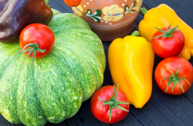 Abóbora verde, tomate, pimenta e jarro em um fundo de madeira preto