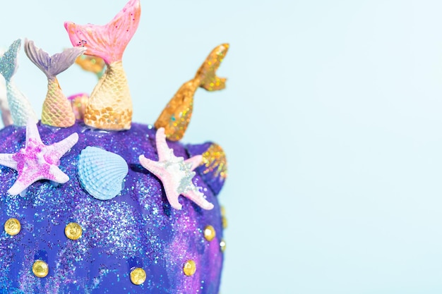 Abóboras artesanais de Halloween decoradas com caudas de sereia, glitter e strass brilhantes em um fundo azul.