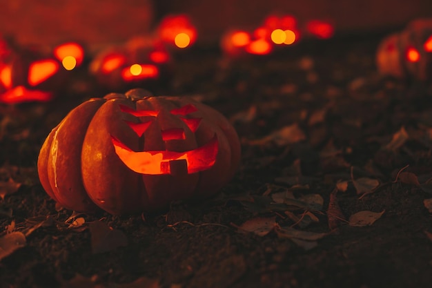 Abóboras assustadoras de Halloween na escuridão no chão entre folhas secas na rua Hallows Eve decoração engraçada abóbora brilhante com velas em fundo escuro ao ar livre perto de casa