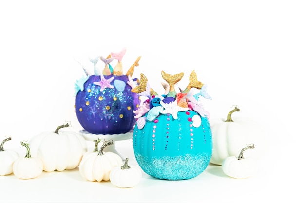 Abóboras de artesanato de halloween decoradas com caudas de sereia, glitter e strass brilhantes em um fundo branco.