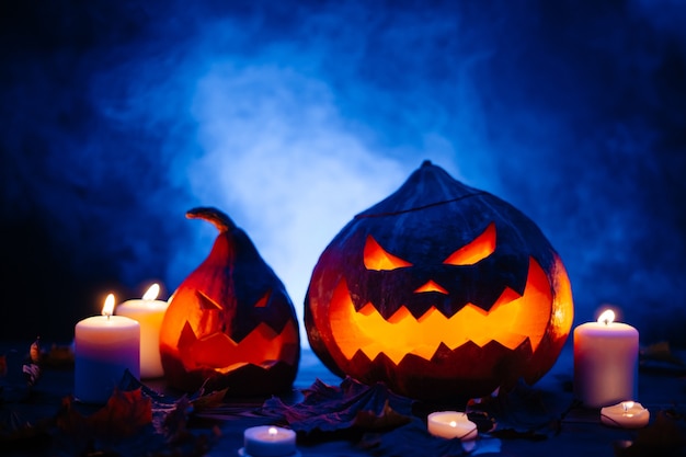 Foto abóboras de halloween com rostos horríveis cortados em um fundo azul escuro com névoa à luz de velas.