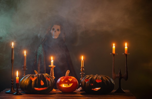 Abóboras de Halloween com velas acesas e morte no manto em fundo escuro