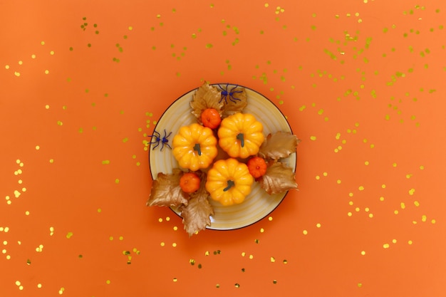 Abóboras em um prato amarelo com aranhas na laranja com confetes dourados.