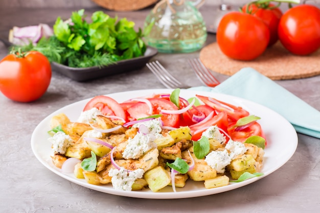 Abobrinha frita com queijo feta, tomate, ervas e cebola em um prato