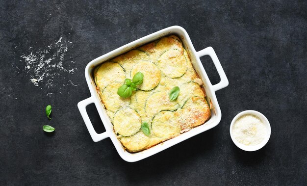 Abobrinha gratinada com molho e parmesão em um fundo escuro de concreto