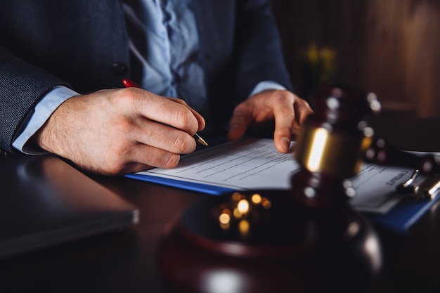 Abogado de hombre que trabaja con contrato en papel. Martillo de madera y libra sobre el escritorio.