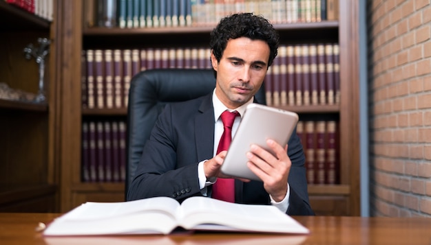 Foto abogado usando una tableta y leyendo un libro en su estudio