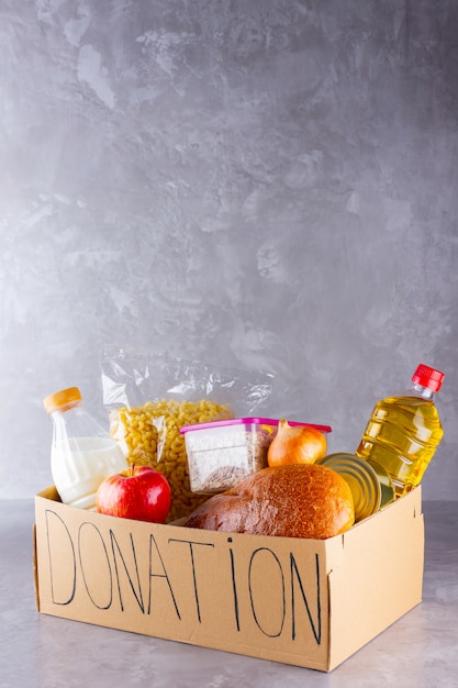 Foto abra a caixa de papelão com óleo, leite, comida enlatada, macarrão e pão. conceito de doação