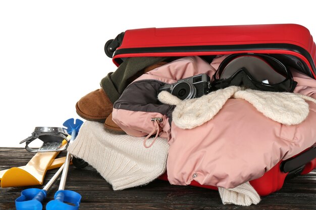 Foto abra a mala com roupas quentes e roupa de esqui na mesa de madeira contra branco. conceito de férias de inverno