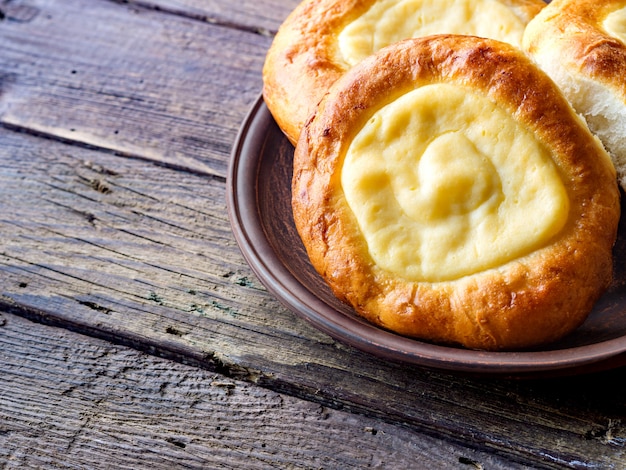 Abra bolos com queijo cottage (vatrushka) deitado em um prato de barro em uma mesa de madeira.