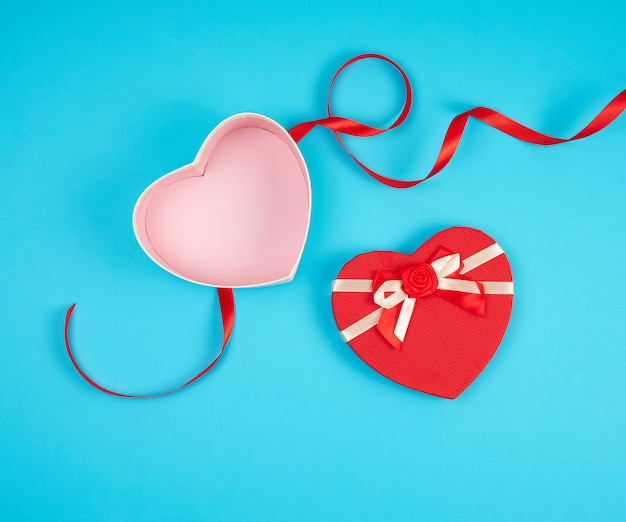 Abra la caja de regalo en forma de corazón rojo con un arco sobre un fondo azul