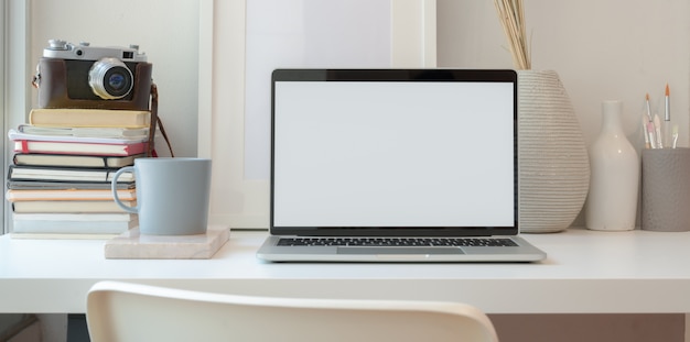 Abra la computadora portátil con pantalla en blanco en un espacio de trabajo mínimo con suministros de oficina