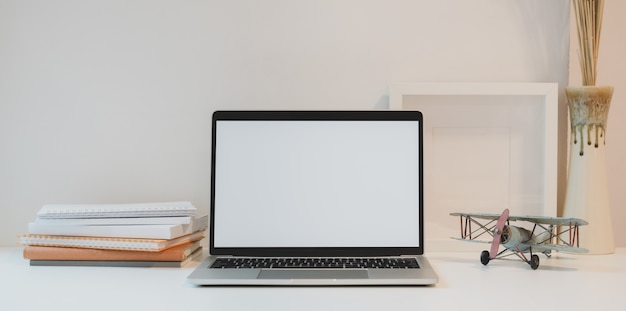 Abra la computadora portátil de pantalla en blanco con una taza de café y suministros de oficina en un lugar de trabajo mínimo