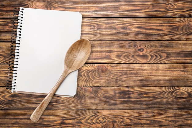 Abra el cuaderno en blanco y la cuchara de madera sobre un fondo de madera