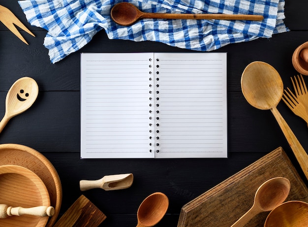 Abra el cuaderno de papel vacío con hojas blancas en una línea en un resorte en medio de artículos de cocina de madera