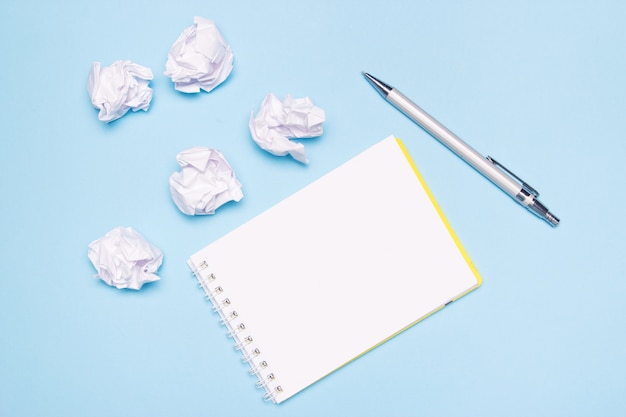 Abra el cuaderno vacío, bolígrafo y bolas de papel arrugado sobre papel azul