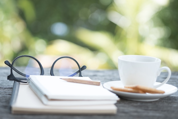 Abra el cuaderno vacío con lápiz, vasos, café negro y galletas. Desenfocar la imagen