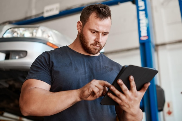 Abra o aplicativo para encontrar um mecânico confiável e confiável perto de você Foto de um mecânico usando um tablet digital enquanto trabalhava em uma oficina de automóveis