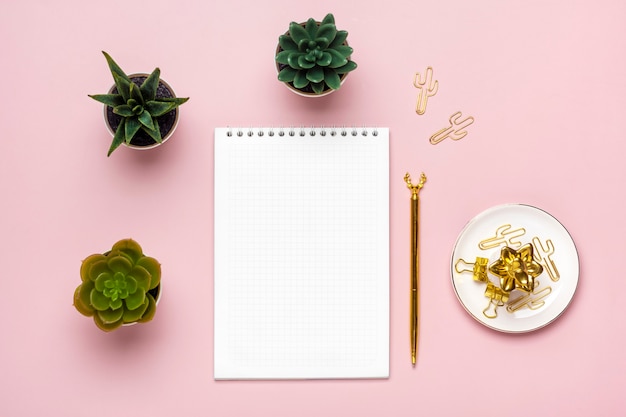 Abra o bloco de notas, suculentas, caneta dourada no fundo rosa, caderno espiral na mesa.