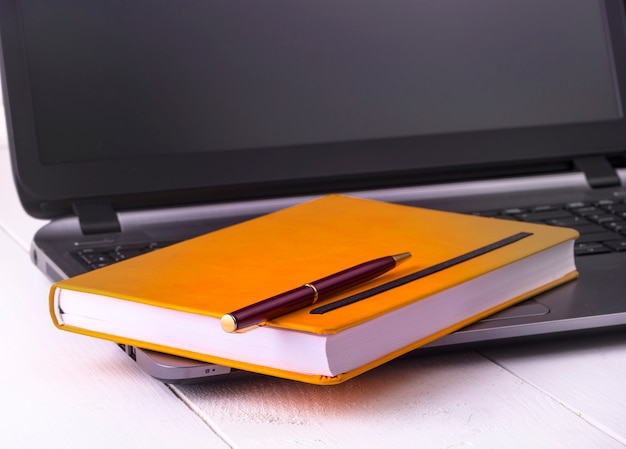 Abra o caderno laranja com um lápis sobre um laptop em meio a fundos de madeira